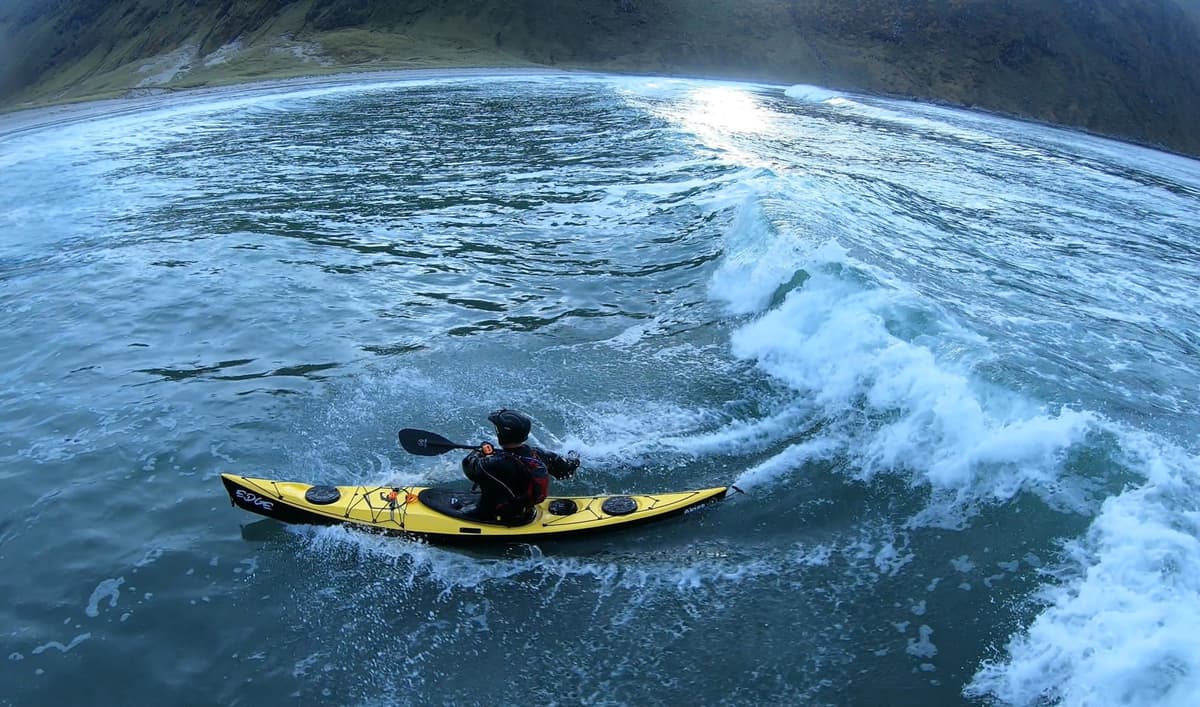 Paddler riding a wave in a yellow sea kayak