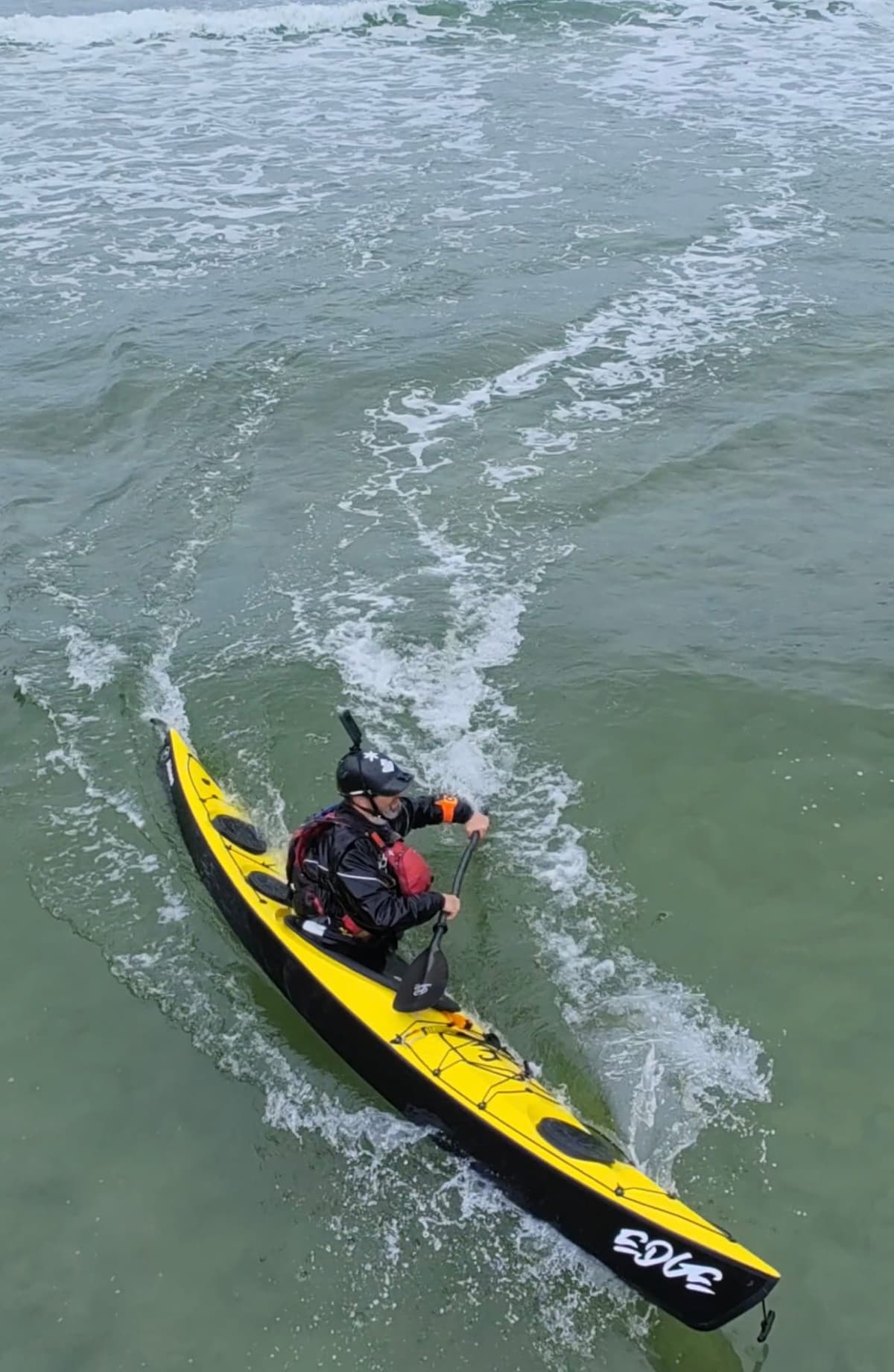 Yellow sea kayak surfing a wave seen from above
