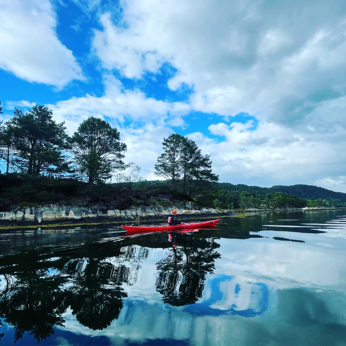Red kayak on a mirror-calm fjord reflecting forest and clouds