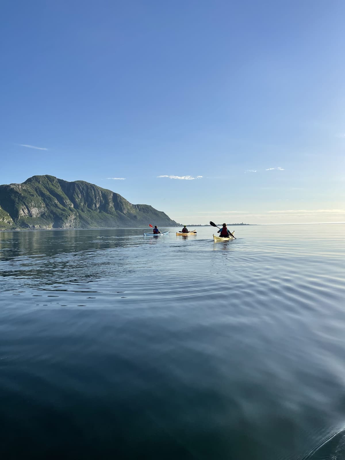 Paddlers beneath a steep mountain on glassy water