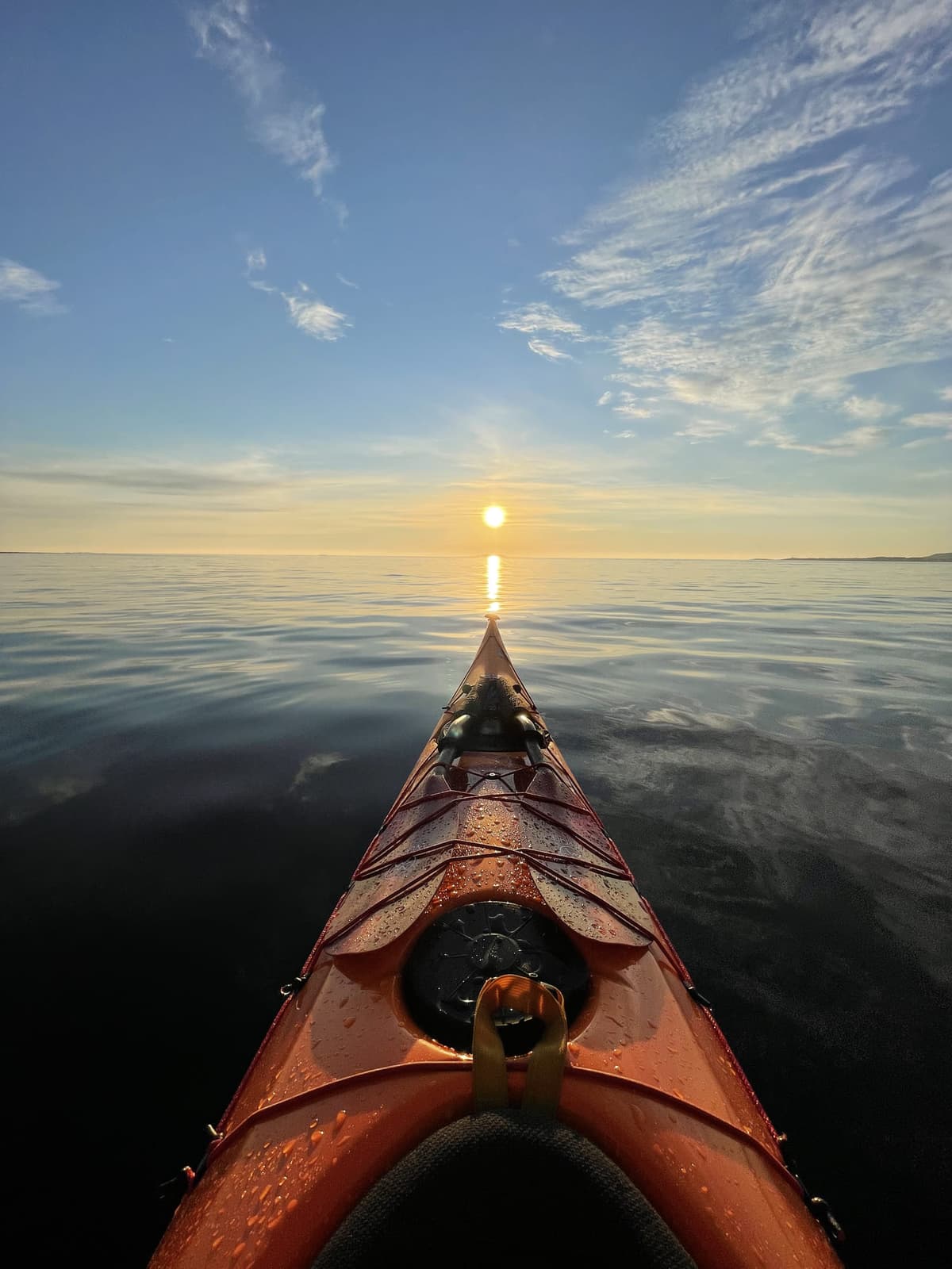 The bow of a sea kayak pointing at the sun setting into the sea