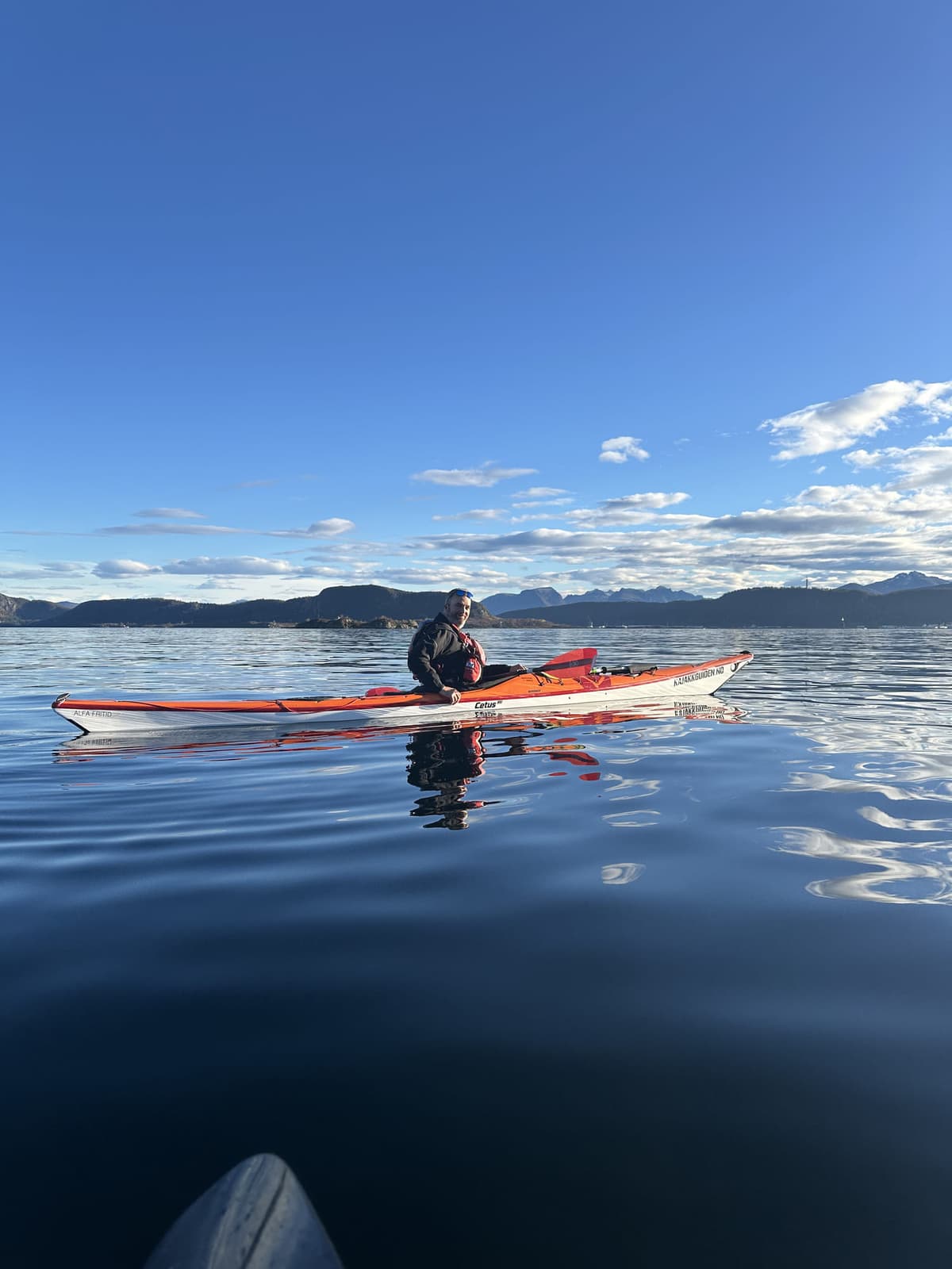 Paddler in a red kayak on a glassy fjord