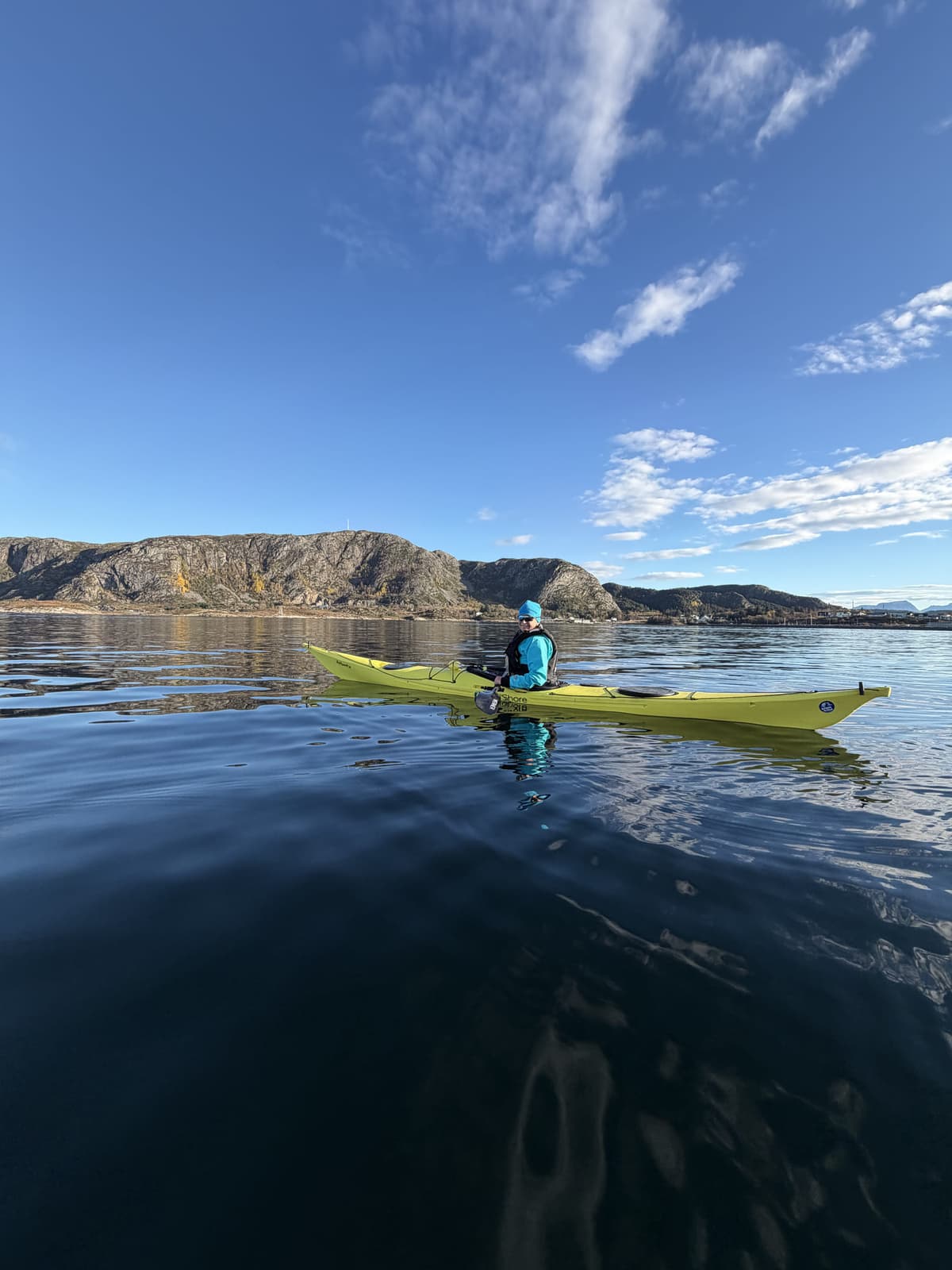 Paddler in a green sea kayak on glassy water in front of the cliff coast